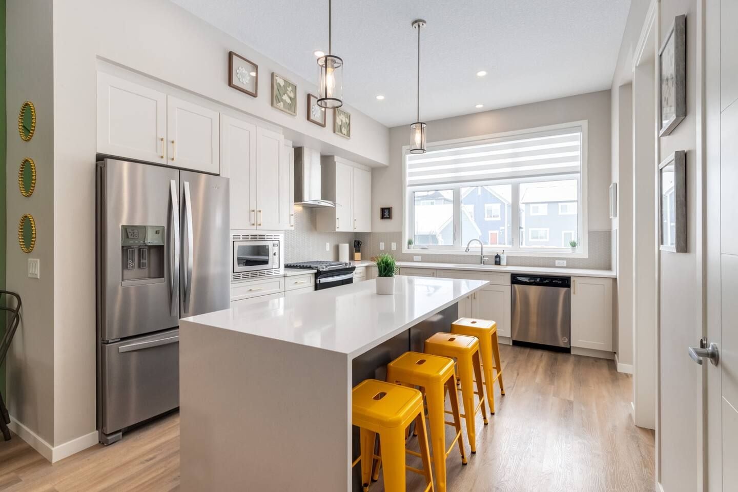 A modern kitchen with stainless steel appliances, a large island, and yellow bar stools.
