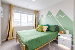Een slaapkamer met een bed, een raam, een muur met een bergdecor en een nachtkastje met een lamp.