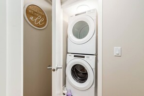 A laundry room with two stacked front-loading washing machines and a wooden sign on the wall. - +Sleeps15 | 2Kitchens | 3 FamilyRooms | 5FullBaths (Calgary)