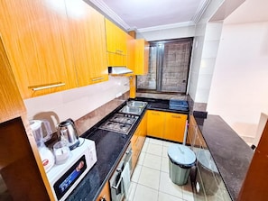 Una cocina pequeña con armarios de madera, cocina a gas, pileta y basurero.