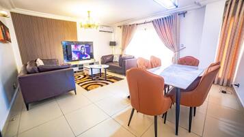 A living room with a sofa, a television, a dining table with chairs, and a patterned rug.