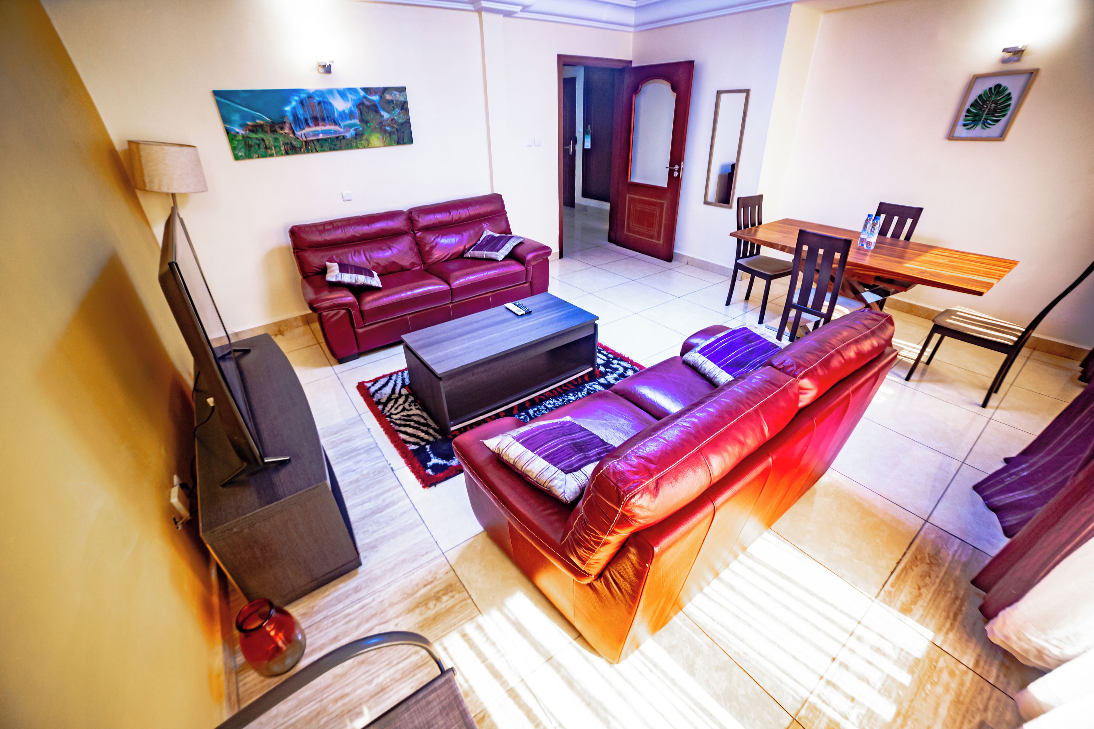 A living room with a red sofa, a coffee table, a TV, and a dining area with a wooden table and chairs.