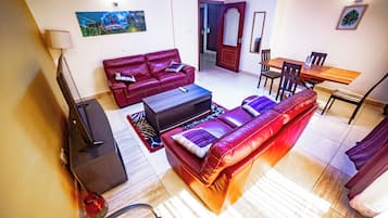 Uma sala de estar com um sofá vermelho, uma mesa de centro, uma televisão e um espaço de refeições com uma mesa e cadeiras de madeira.