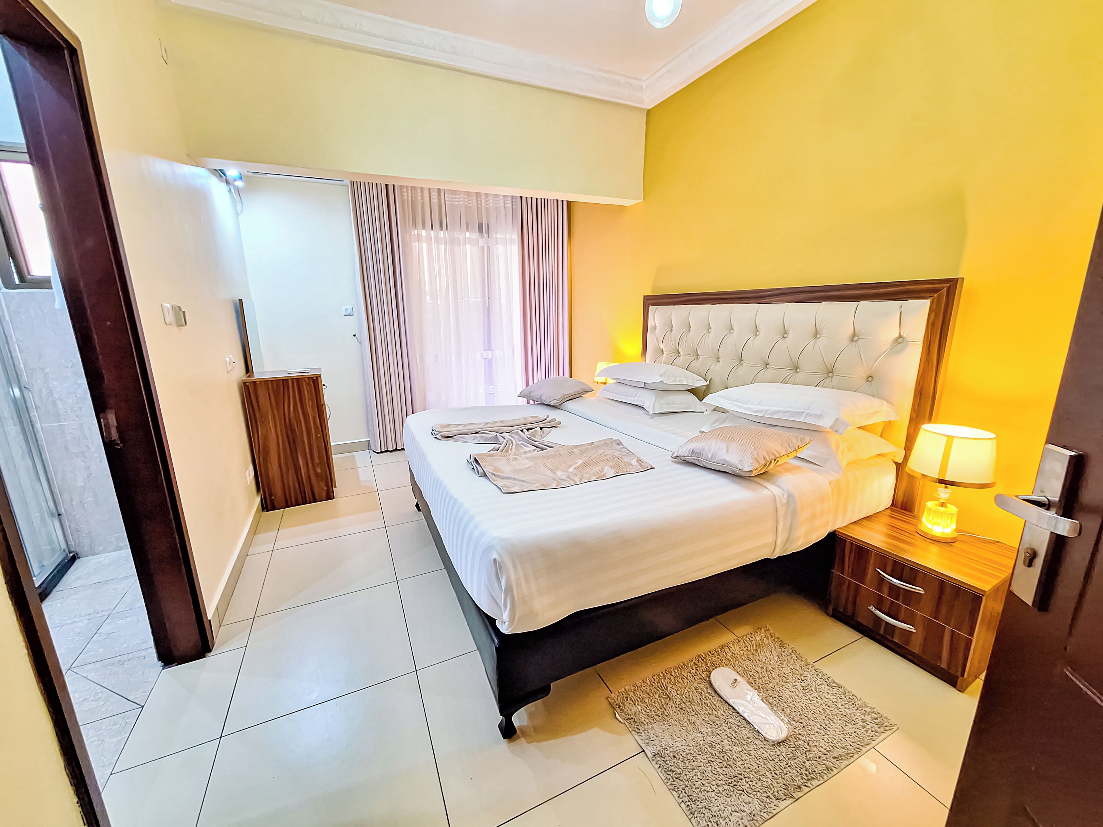 Habitación de hotel con una cama grande, mesitas de noche, una lámpara y la puerta del baño.