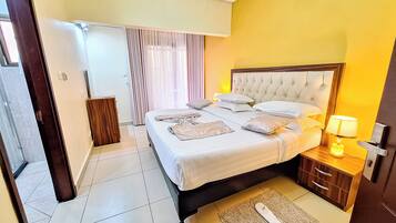 Habitación de hotel con una cama grande, mesitas de noche, una lámpara y la puerta del baño.
