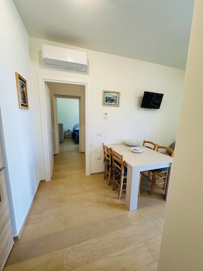 Uma área de refeições com mesa, cadeiras, televisão na parede e um aparelho de ar condicionado.