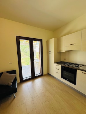 Cozinha moderna com fogão a gás, forno e porta de vidro deslizante para área externa.