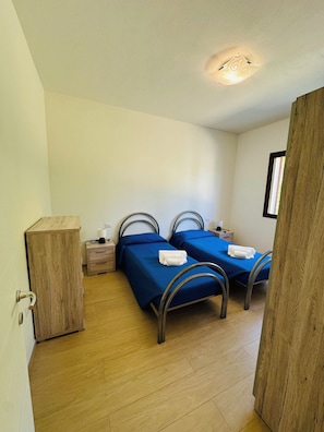 Quarto com duas camas, guarda-roupa de madeira, mesas de cabeceira e luminária no teto.