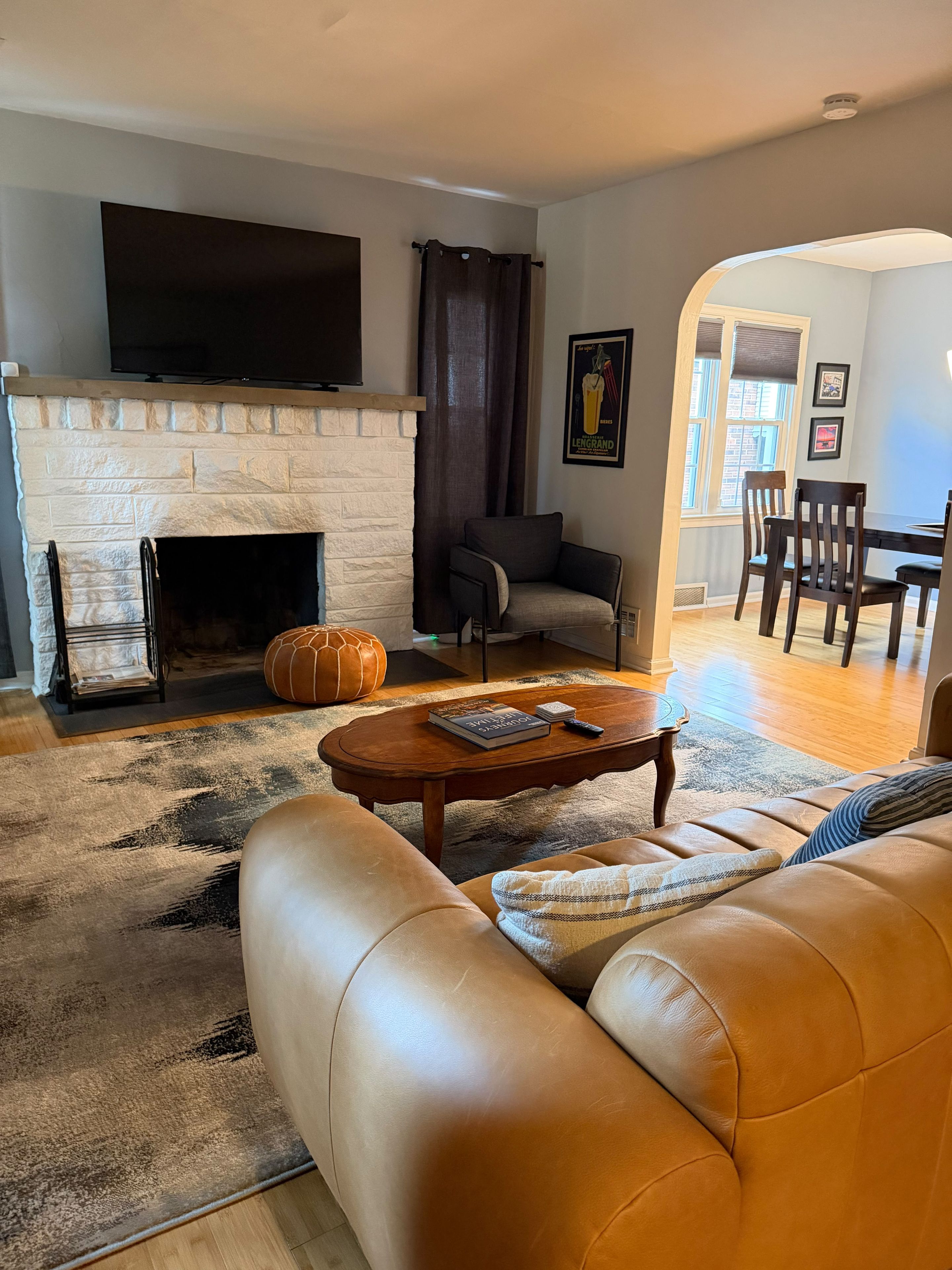 A living room with a fireplace, leather sofa, coffee table, and a flat-screen TV mounted above the fireplace.