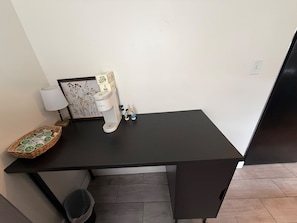 A small, dark-colored desk with a coffee machine, a lamp, a framed picture, and a basket of items. - Hoosier House - Cozy 2BR Indy Stay Near Everything (Indianapolis)