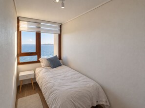 A bedroom with a bed, a nightstand, and a window with a view of the sea. - Cozy Apartment with a Spectacular Ocean View in Puerto Montt, Pelluco Beach (Puerto Montt)