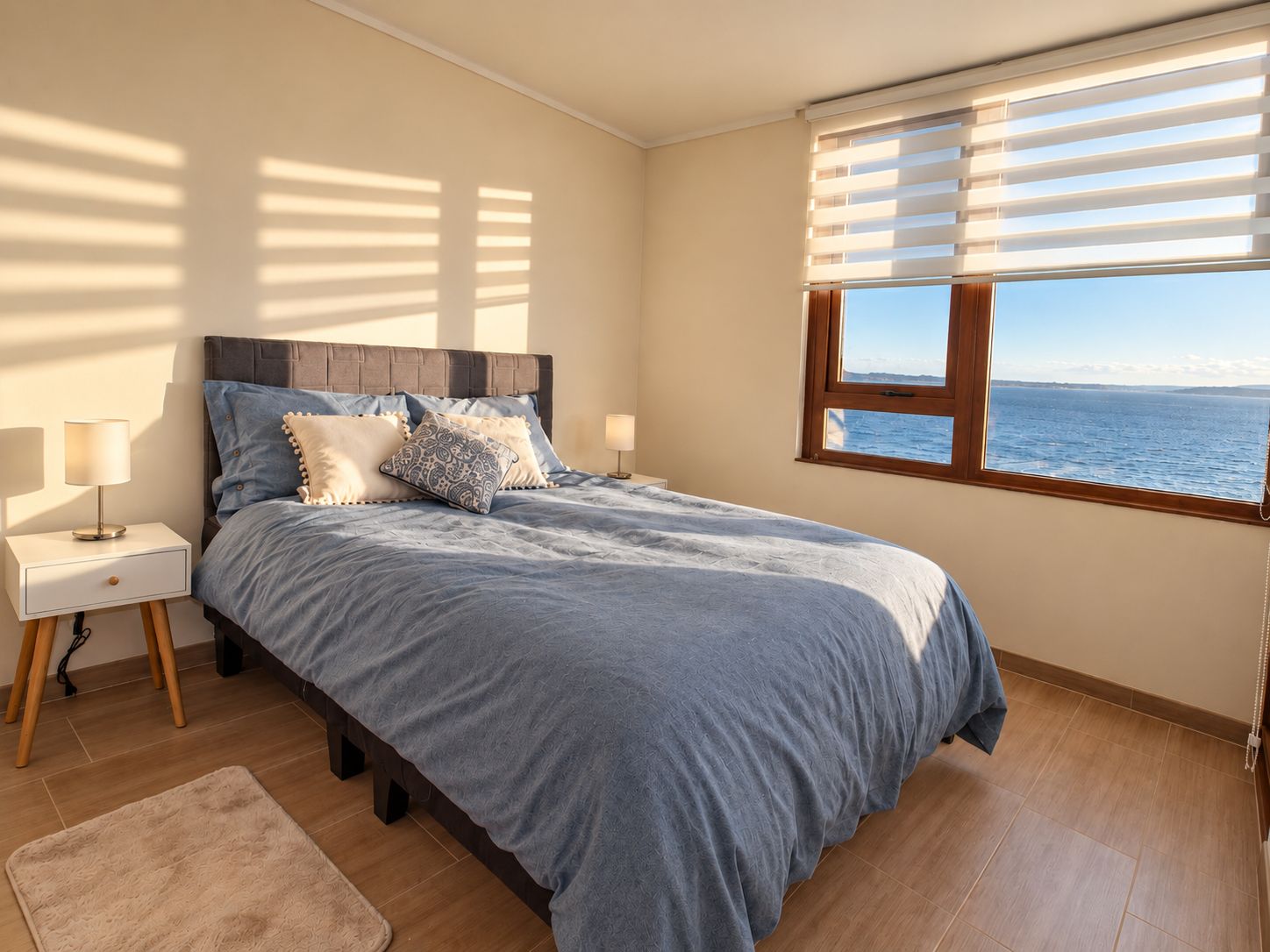 Une chambre à coucher avec un lit, des lampes de chevet, une table de chevet, une fenêtre avec des stores et une vue sur la mer.