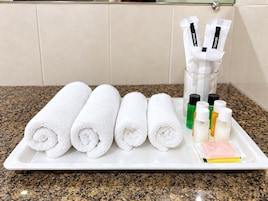 A tray with rolled white towels and toiletries including bottles and a pink packet.