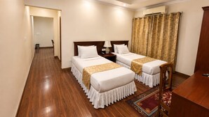 A hotel room with two beds, a desk, a chair, a nightstand, a lamp, and a window with curtains. - The Orchid Phuentsholing (Phuntsholing)