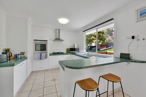 Eine moderne Küche mit weißen Schränken, einem eingebauten Ofen, einem Gasherd und einem großen Fenster mit Blick ins Freie.