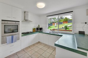 Eine moderne Küche mit weißen Schränken, einem Gasherd, einem Backofen, einer Mikrowelle und einem großen Fenster mit Blick auf einen Garten.