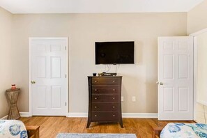 Ein Schlafzimmer mit einem Bett, einer Kommode, einem an der Wand montierten Fernseher und zwei Türen.