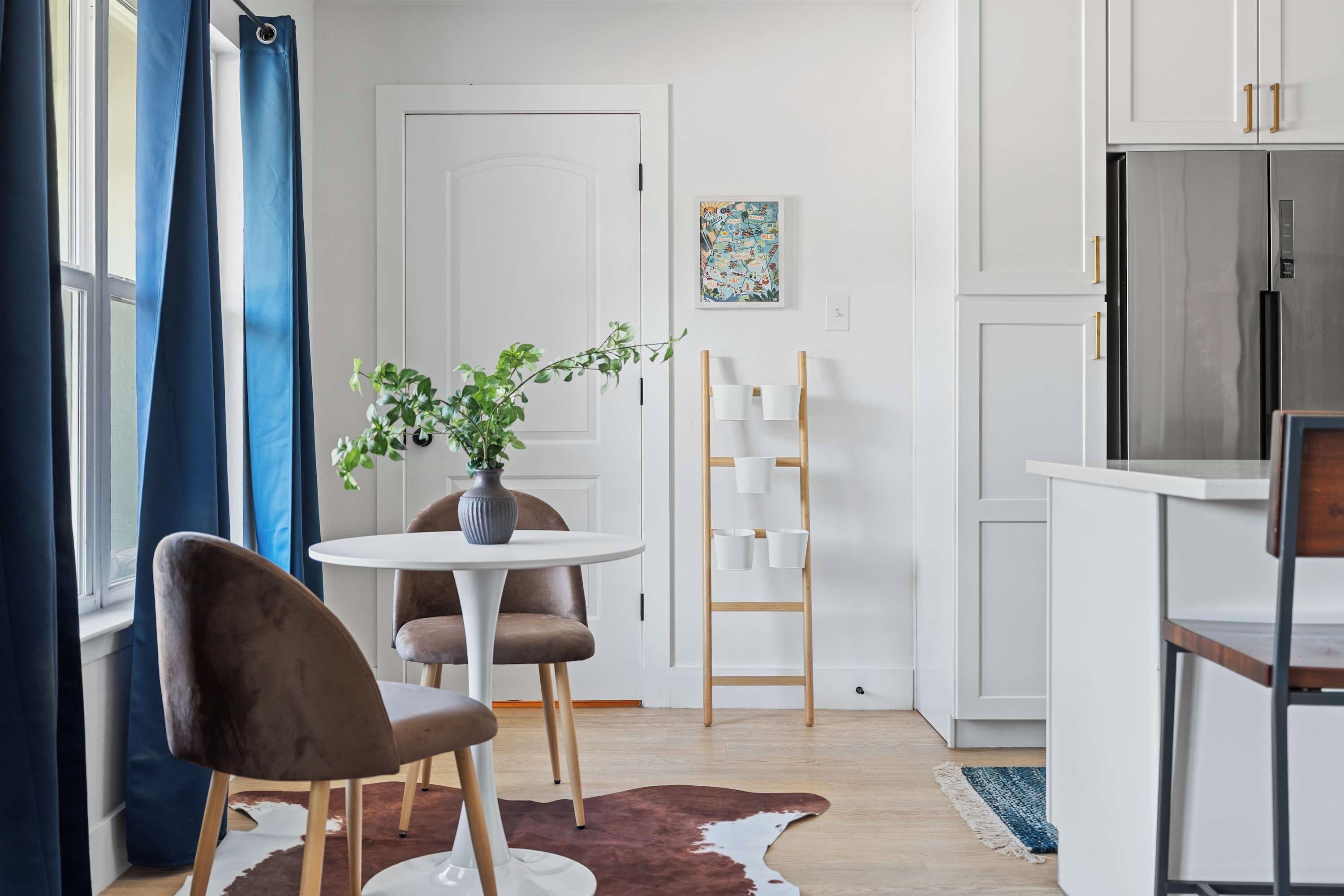 Een moderne keuken met witte kasten, een roestvrijstalen koelkast, en een eethoek met een ronde tafel en twee stoelen.