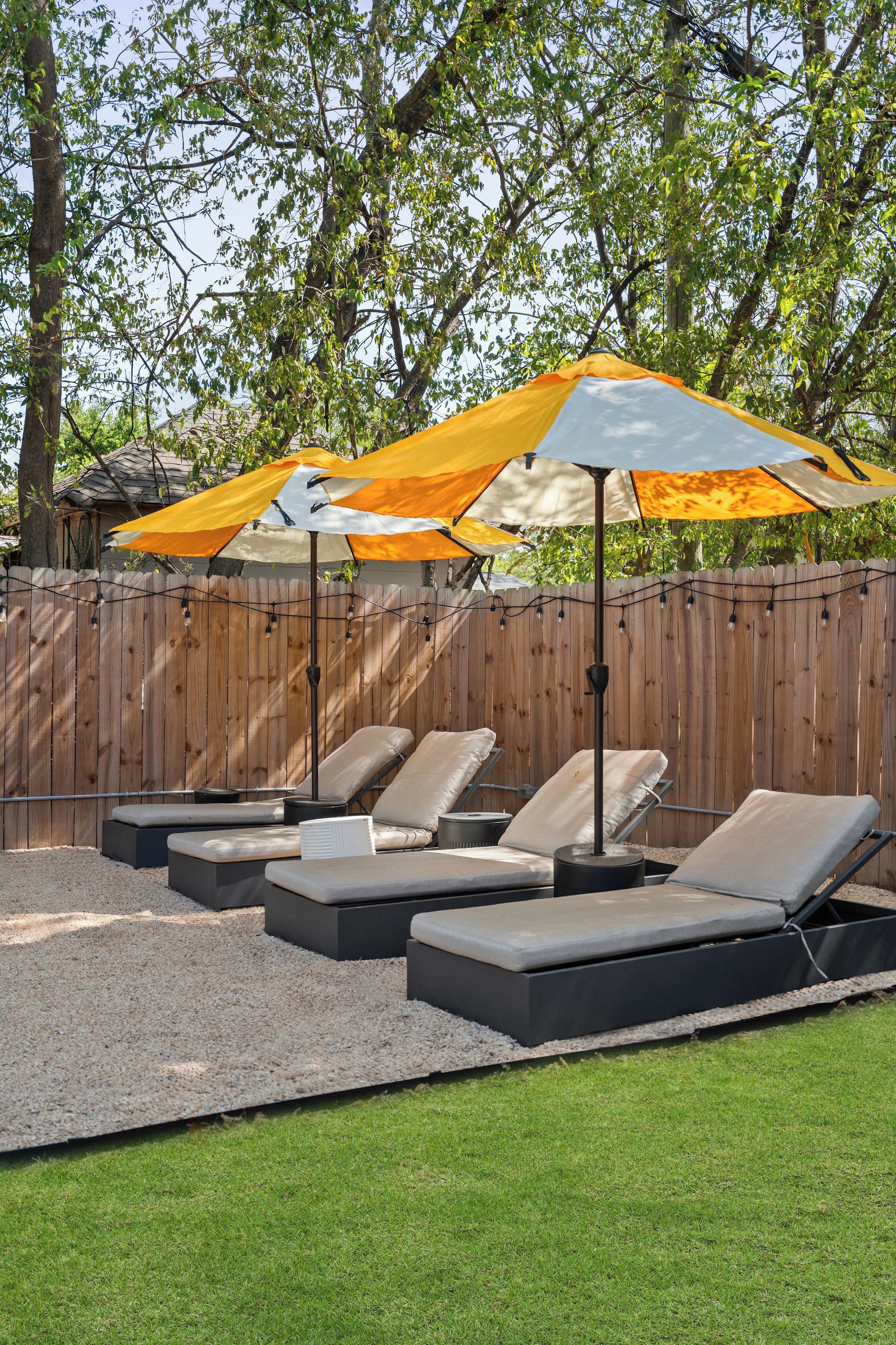 A backyard with a wooden fence, outdoor seating with cushions, and two umbrellas providing shade.