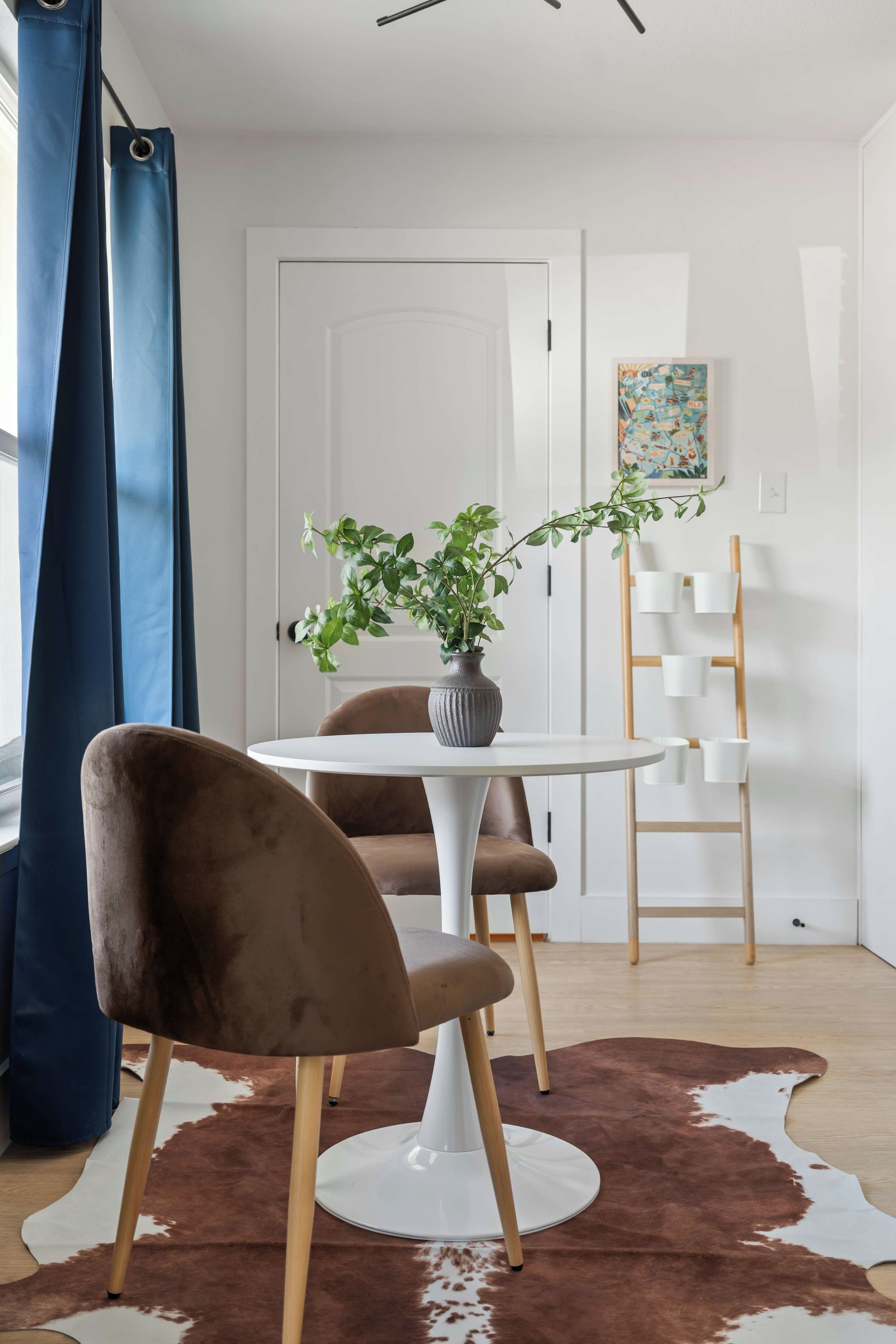 Un comedor moderno con una mesa redonda blanca, una silla tapizada marrón, una planta en maceta y una alfombra de piel de vaca.