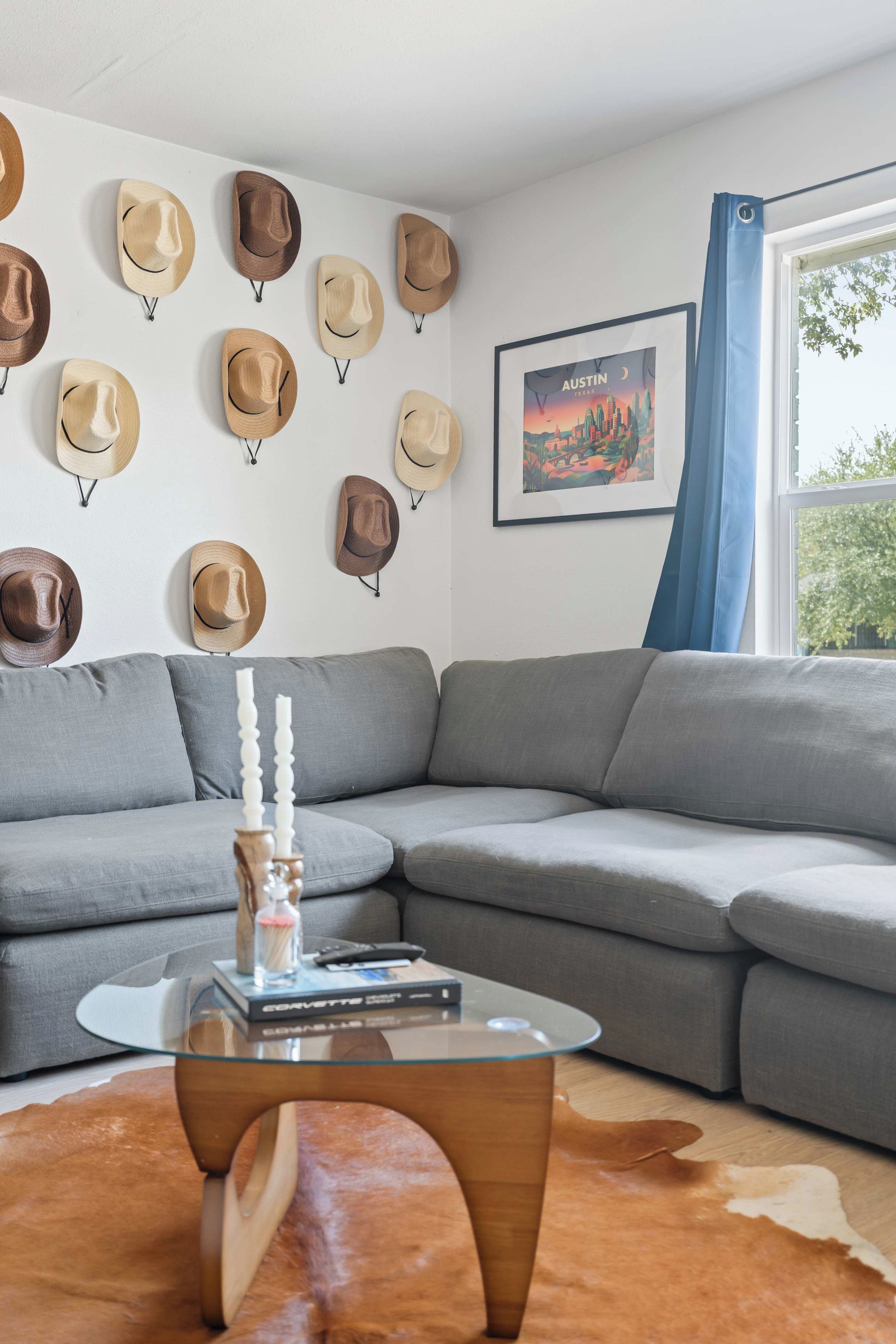 Una sala de estar moderna con un sofá modular, una mesa de centro de vidrio y una pared decorada con sombreros.