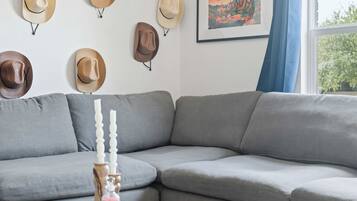 Una sala de estar moderna con un sofá modular, una mesa de centro de vidrio y una pared decorada con sombreros.