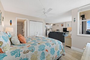 A bedroom with a bed, a ceiling fan, a bathroom, a kitchen, and a living area. - Estero Beach & Tennis 802c - Beach Sunrise (Fort Myers Beach)