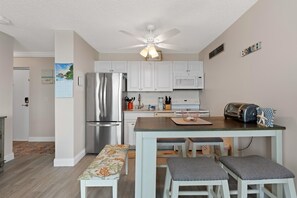 A modern kitchen with white cabinets, a stainless steel refrigerator, a microwave, and a toaster. There is a wooden island with stools and a bench. - Estero Beach & Tennis 802c - Beach Sunrise (Fort Myers Beach)
