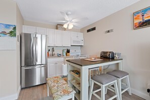 Eine kompakte Küche mit Kühlschrank, Mikrowelle und Toaster. Es gibt eine kleine Kücheninsel mit Barhocker und einen Kalender an der Wand.