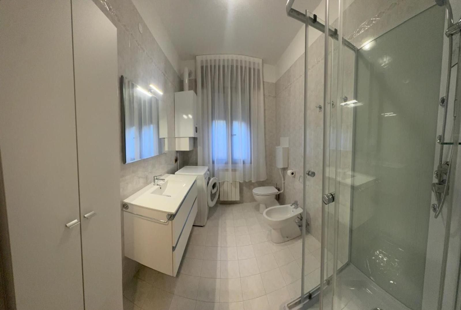 Ein modernes Badezimmer mit einer Duschkabine aus Glas, einer integrierten Waschmaschine, einer Toilette und einem Bidet.