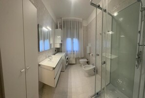 Ein modernes Badezimmer mit einer Duschkabine aus Glas, einer integrierten Waschmaschine, einer Toilette und einem Bidet.