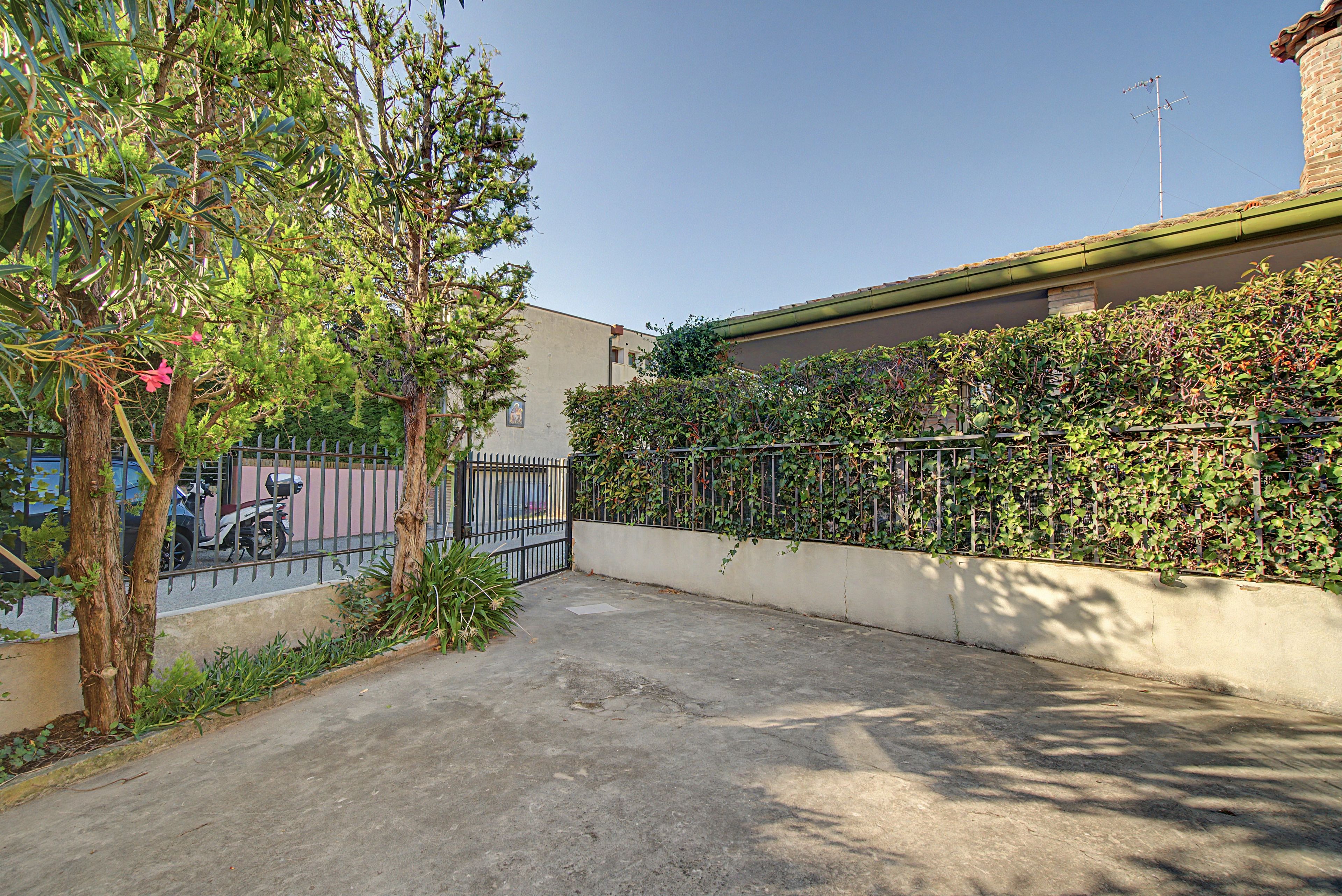 A paved courtyard with a metal fence, a tree, and a building with a brick wall and a green awning.