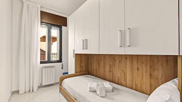 Een slaapkamer met een bed, witte gordijnen, een houten hoofdbord en witte kasten.