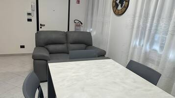 Een moderne kamer met een grijze bank, een witte tafel en een klok aan de muur.