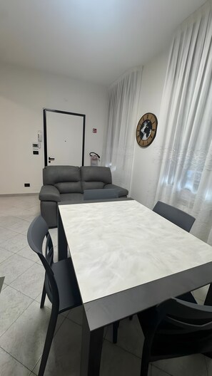 Quarto moderno com sofá cinzento, uma mesa branca e um relógio na parede.