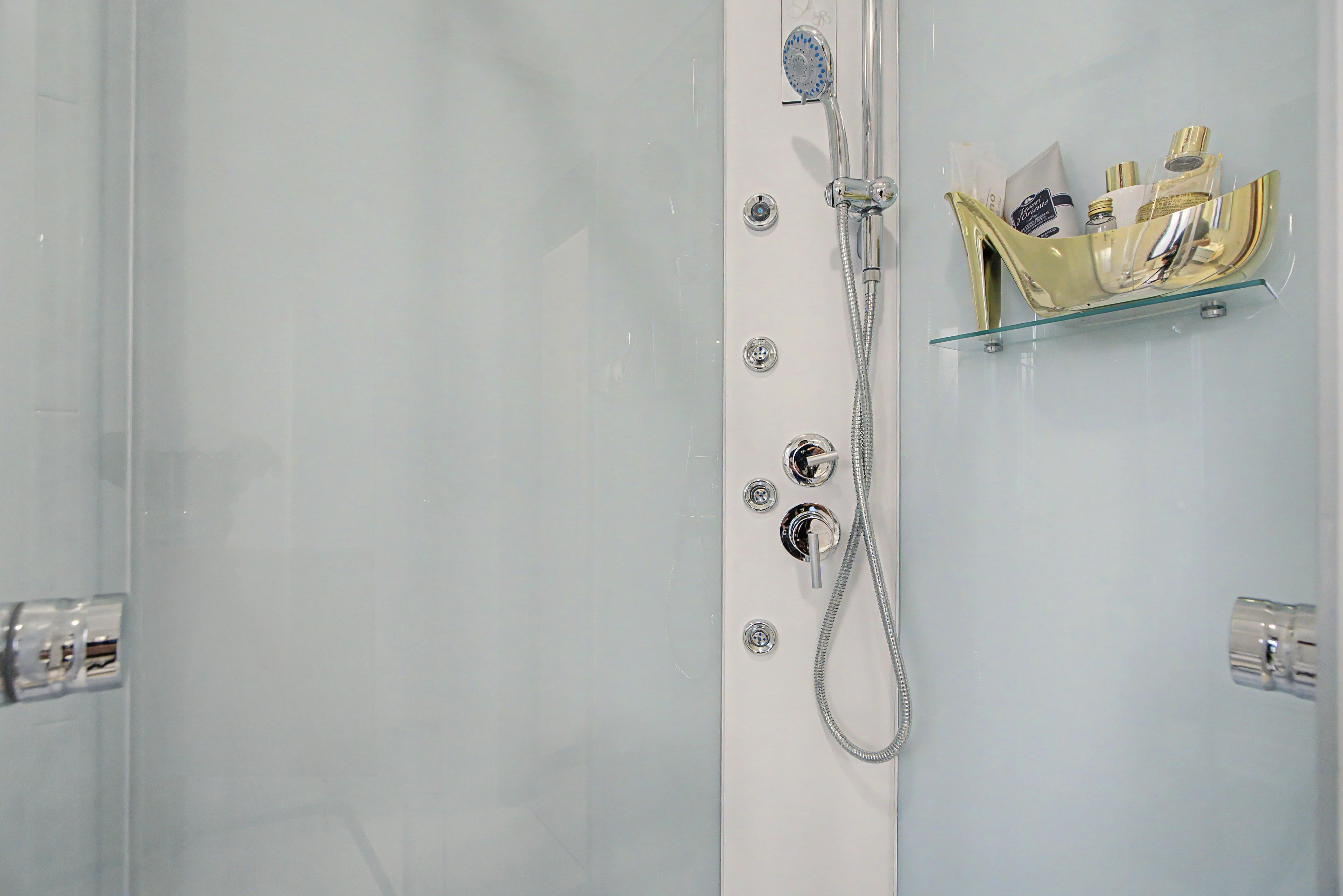 A shower with a handheld showerhead and a glass shelf with toiletries.