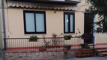A residential building with a balcony, potted plants, and a concrete ground.