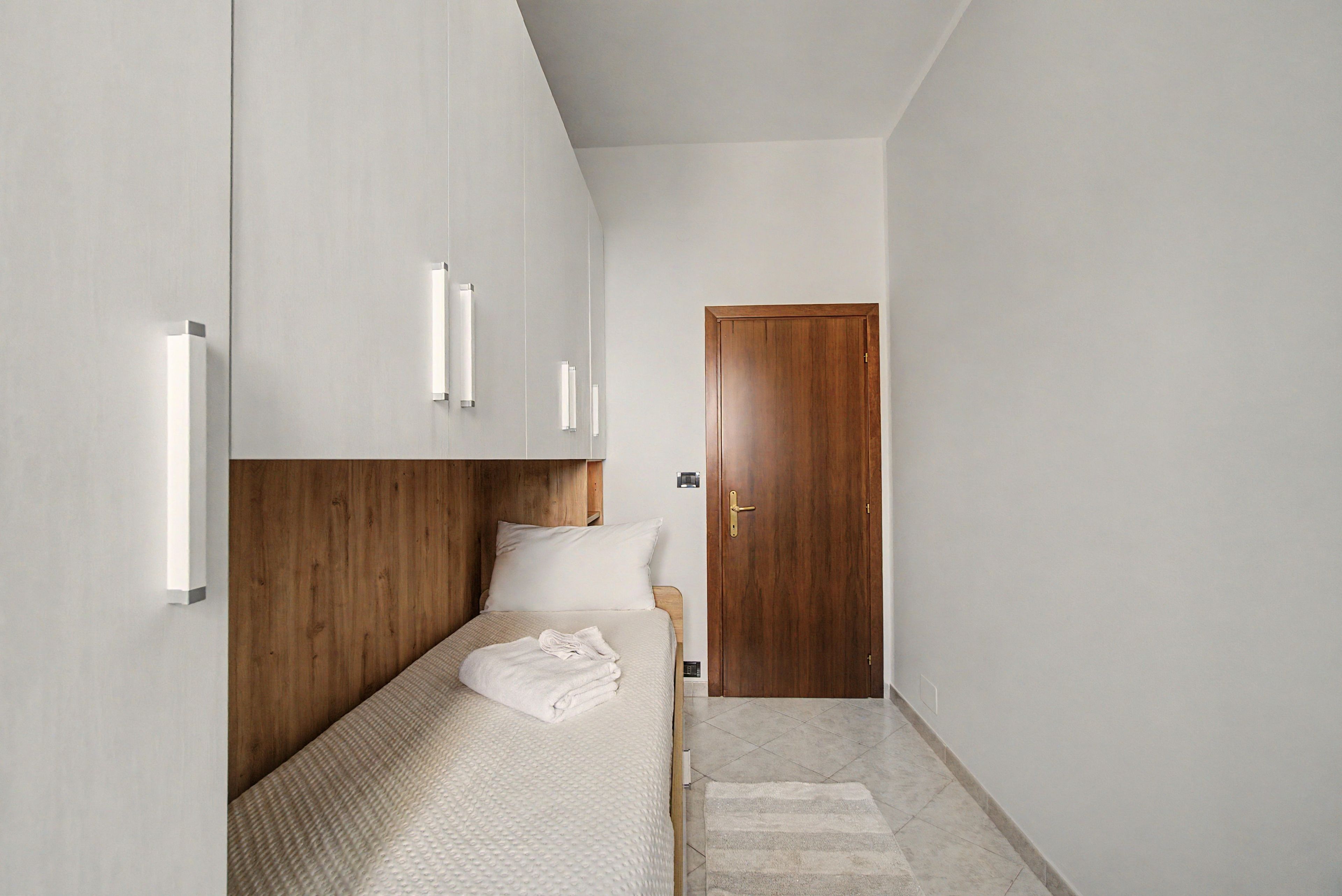 Ein Schlafzimmer mit einem Bett, einem hölzernen Kopfteil, einer Tür und einem kleinen Fenster.