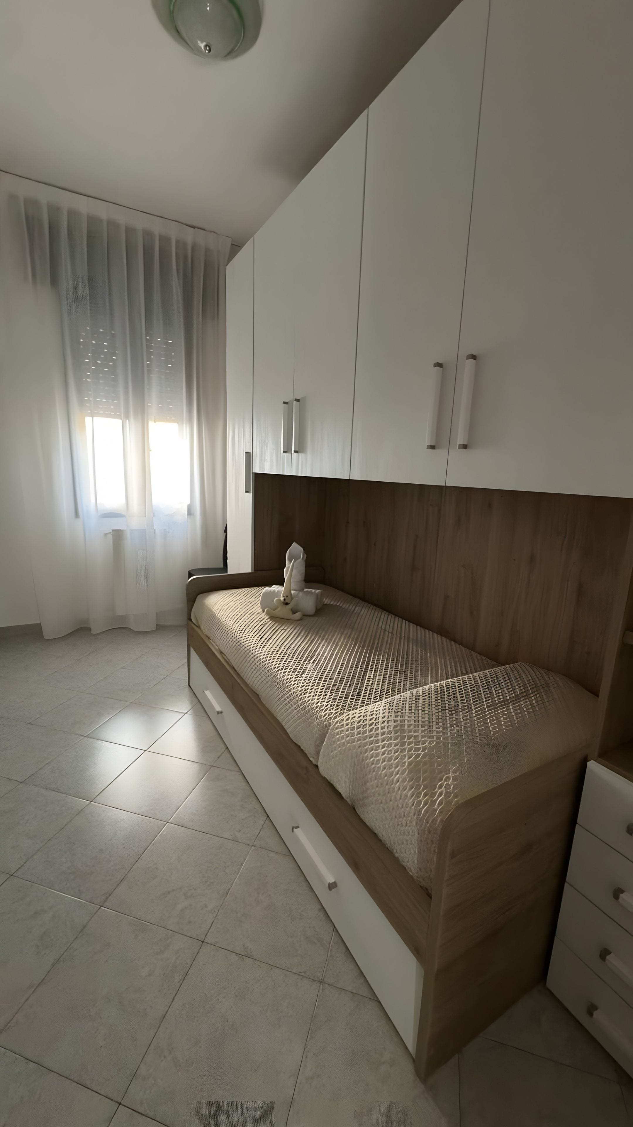 Een slaapkamer met een bed, nachtkastje, dressoir en een raam met gordijnen.