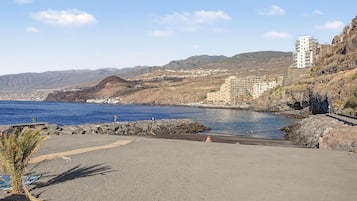 Une route côtière bordée d’une côte rocheuse, avec une mer bleue et limpide et, en arrière-plan, un paysage montagneux.