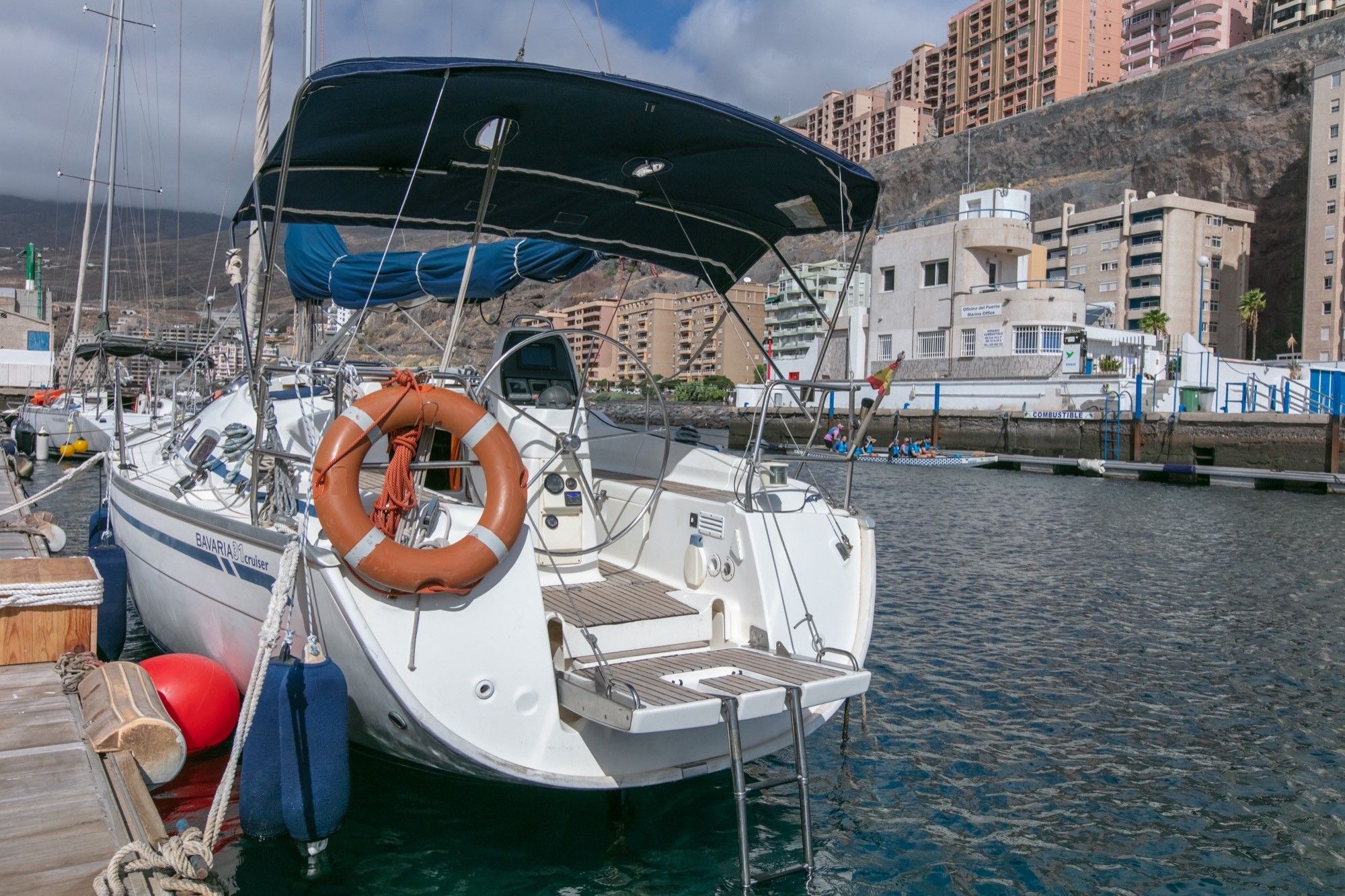 A boat docked at a marina with a lifebuoy attached, a steering wheel, and a canopy.
