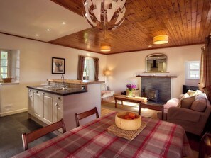 A cozy interior with a kitchen, dining area, and living space, featuring wooden beams, a fireplace, and a large window. - Mauldslie Hill Cottage - Sleeps 6 and Pet Friendly (Gorebridge)