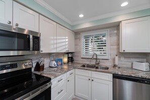 A modern kitchen with white cabinetry, stainless steel appliances, and a marble countertop. - Nautilus 114 by Nautilus Vacations-Beachfront Condo, Pool, Recreation Court (Holmes Beach)
