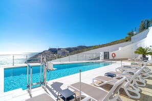 A poolside area with a clear view of the sea, lounge chairs, and a lifebuoy. - Apartment in Nerja With Sea Views & Pool (Nerja)