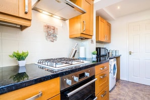Een moderne keuken met houten kastjes, een roestvrijstalen afzuigkap, een inbouwoven en een vaatwasser.
