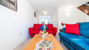 A living room with a wooden coffee table, red and blue sofas, and a fruit bowl.