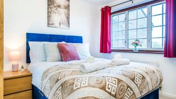 Una cama bien hecha con una colcha estampada, una lámpara de noche y una ventana con cortinas.