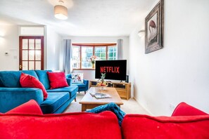 Una sala de estar con un sofá azul, cojines rojos, una mesa de centro de madera y un televisor que muestra el logotipo de Netflix.