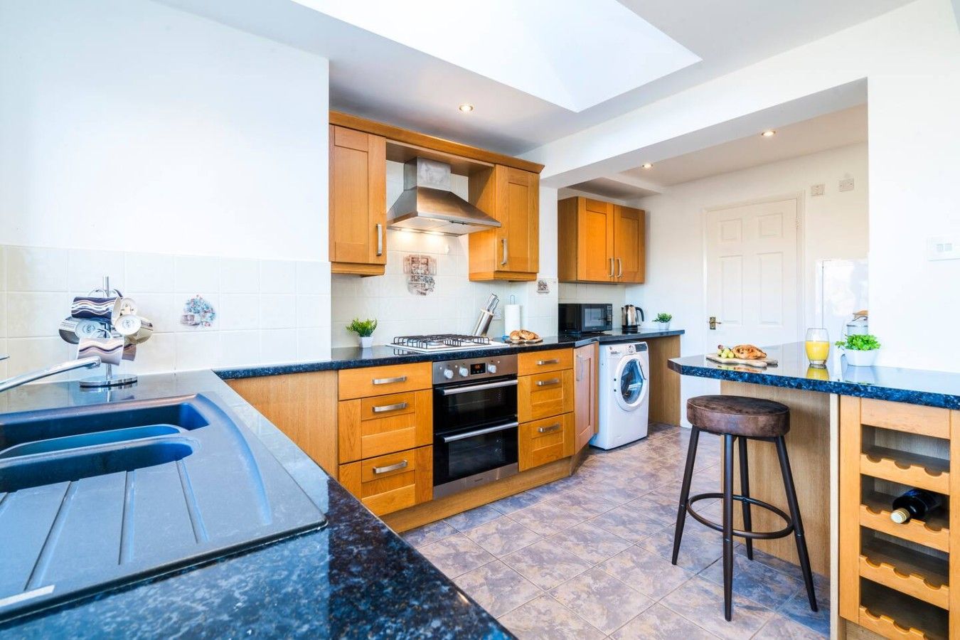 A modern kitchen with wooden cabinets, a built-in oven, a washing machine, and a bar stool.