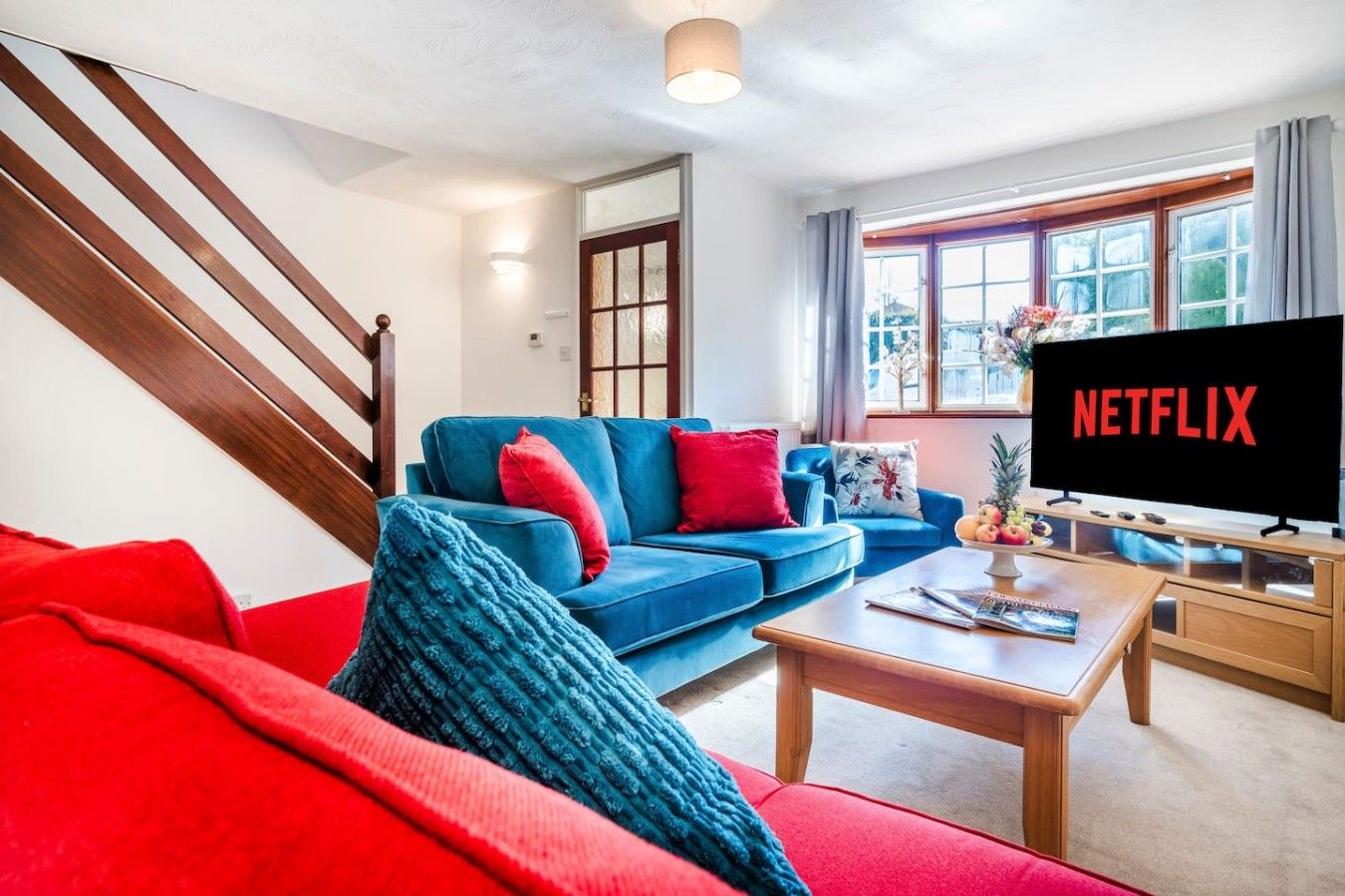 Un soggiorno con un divano blu, cuscini rossi, un tavolino in legno e un televisore che mostra 'NETFLIX'.